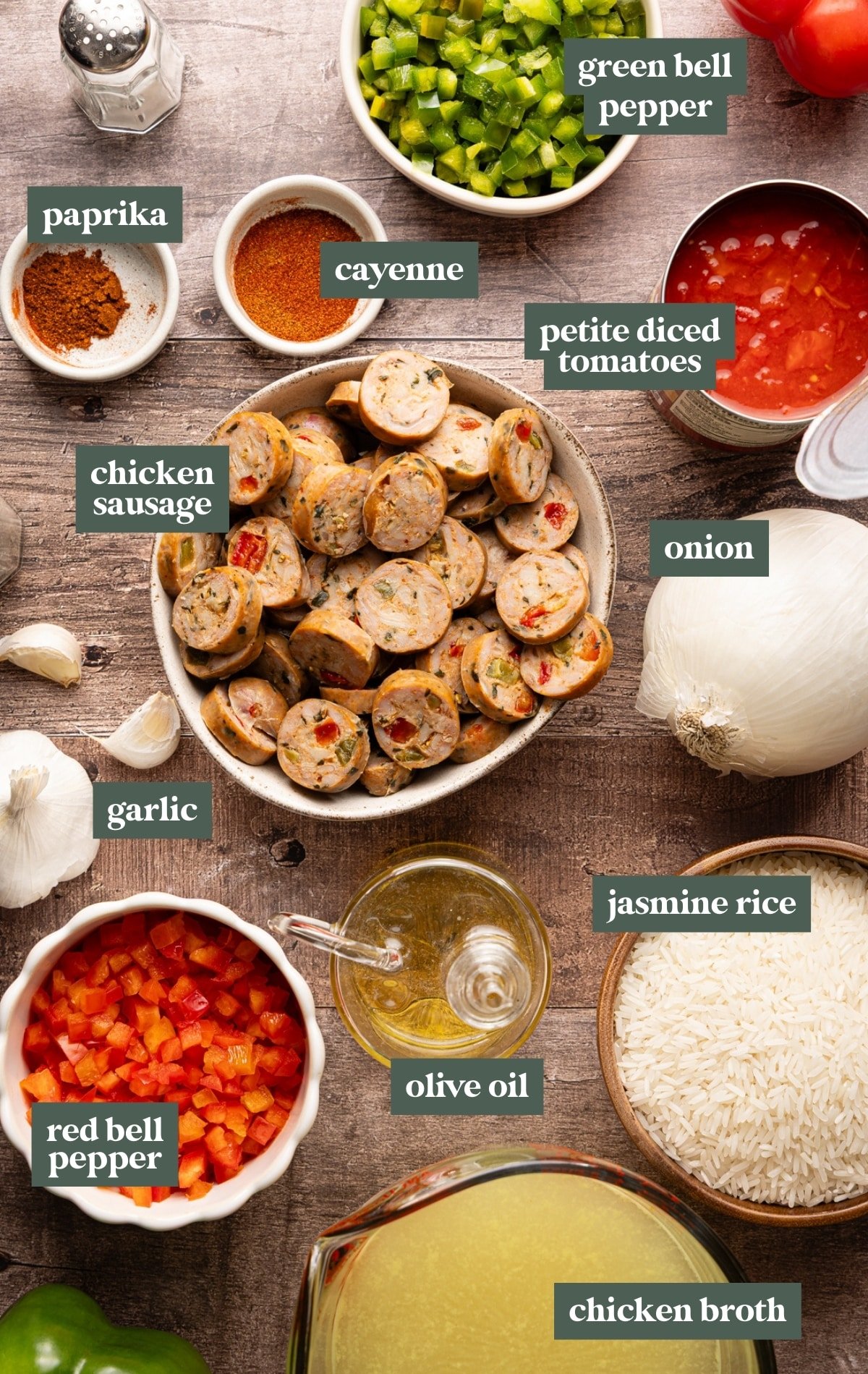 Overhead view of sausage and peppers skillet ingredients including chicken sausage, jasmine rice, onion, garlic, red and green bell peppers, paprika, cayenne pepper, diced tomatoes, olive oil, and chicken broth.