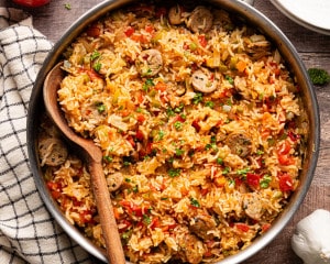 Chicken broth poured into the skillet with sausage, rice, tomatoes, and vegetables before simmering.