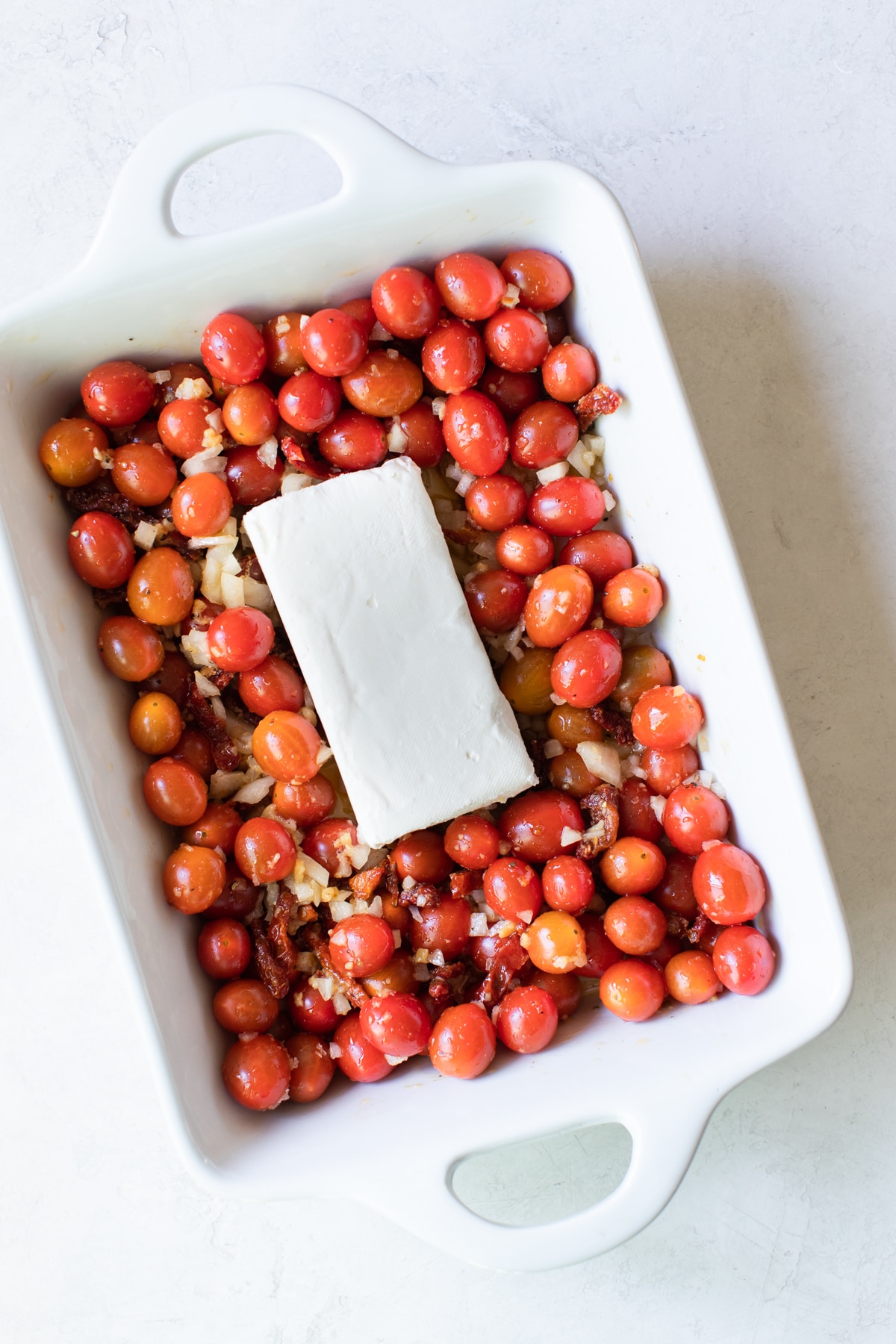 white baking dish with cherry tomatoes, garlic, and a block of cream cheese