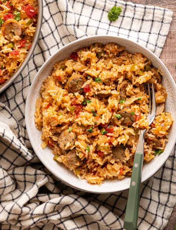 Serving bowl filled with sausage, peppers, and rice, garnished with parsley and placed on a neutral kitchen towel.