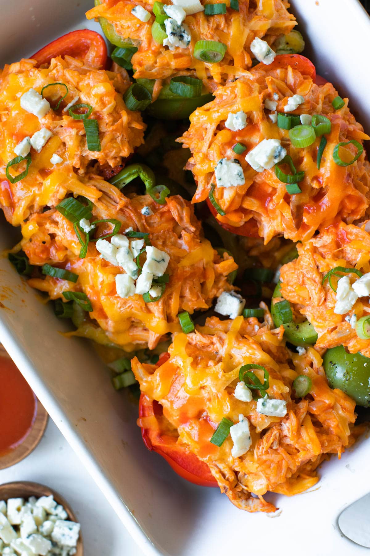 chicken stuffed bell peppers in a white casserole dish topped with bleu cheese and green onions