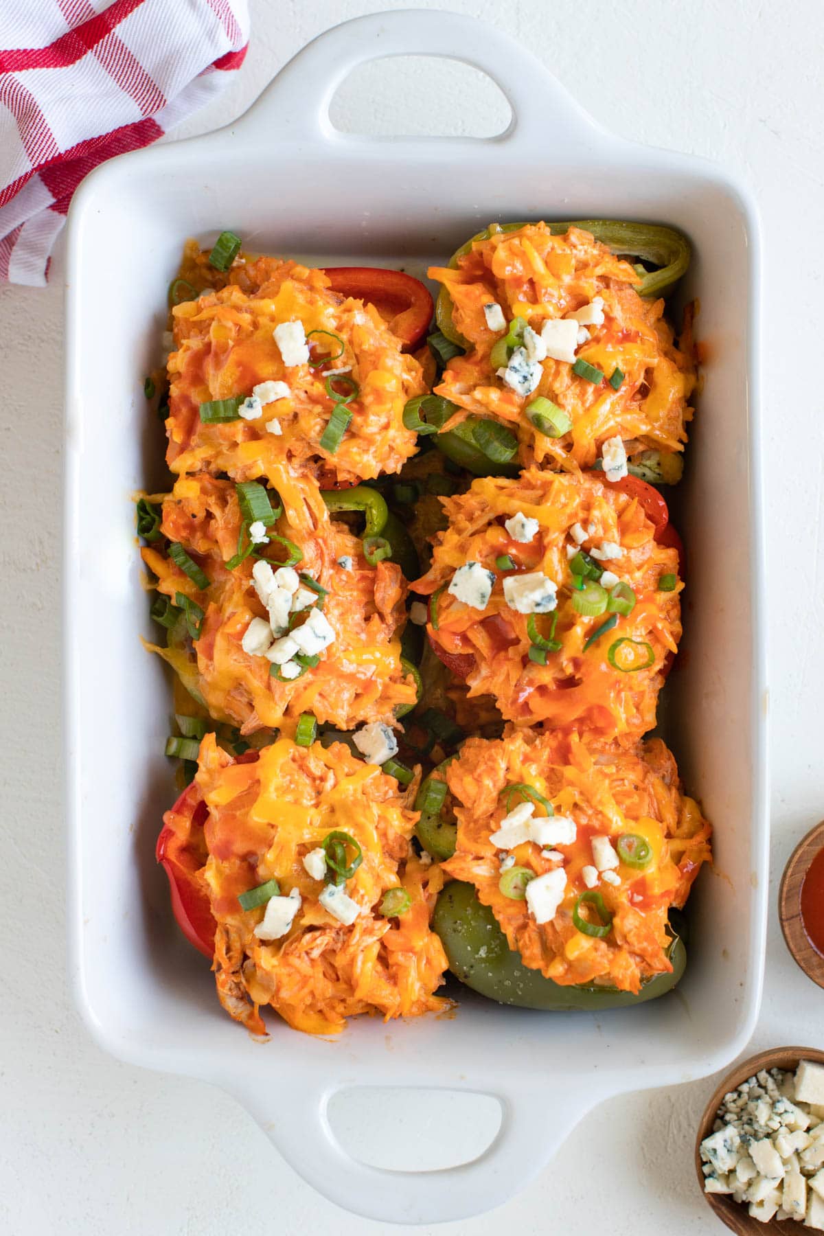 chicken stuffed bell peppers in a white casserole dish topped with bleu cheese and green onions