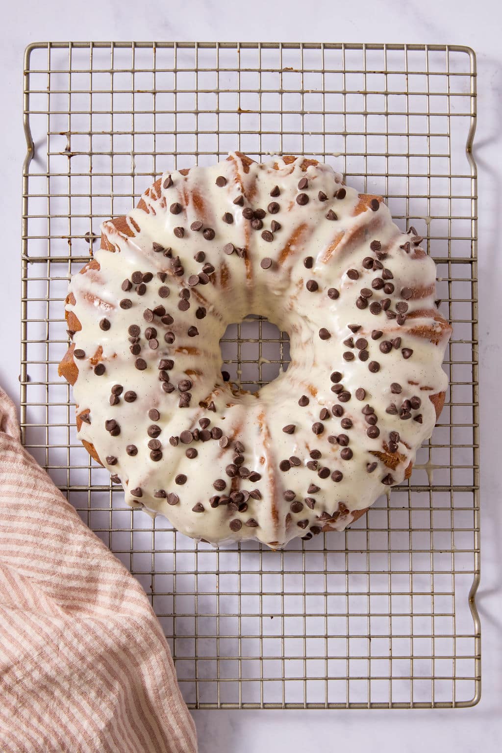 Overhead view of a chocolate chip Bundt cake covered with vanilla bean glaze and sprinkled with mini chocolate chips, resting on a wire cooling rack.