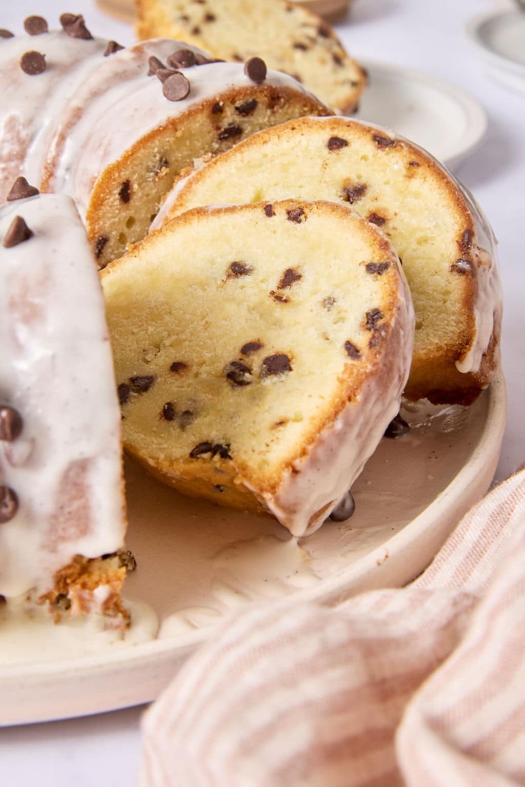Overhead view of a glazed chocolate chip Bundt cake on a serving platter with several slices cut and fanned out beside it, served with a cup of coffee.