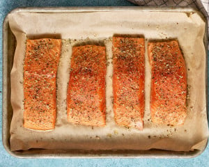 Raw salmon fillets seasoned with herbs, onion powder, salt, and pepper arranged on a parchment-lined baking sheet.