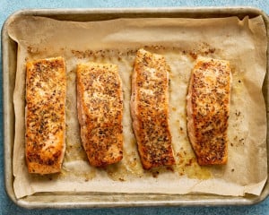 Cooked Mediterranean salmon fillets baked until golden and flaky on a parchment-lined baking sheet.
