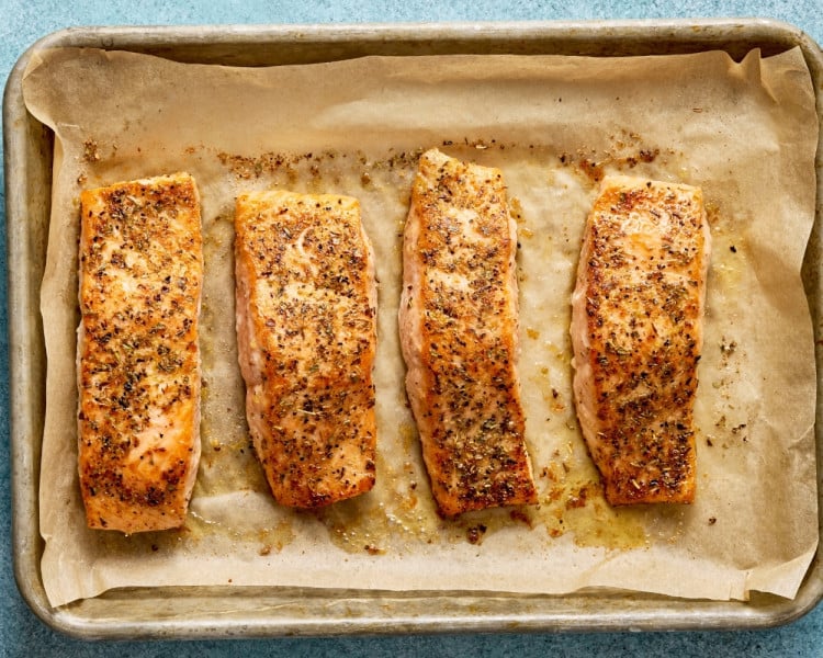 Cooked Mediterranean salmon fillets baked until golden and flaky on a parchment-lined baking sheet.