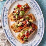 Mediterranean salmon fillets topped with avocado, tomato, olives, and feta arranged on a blue-and-white serving platter.