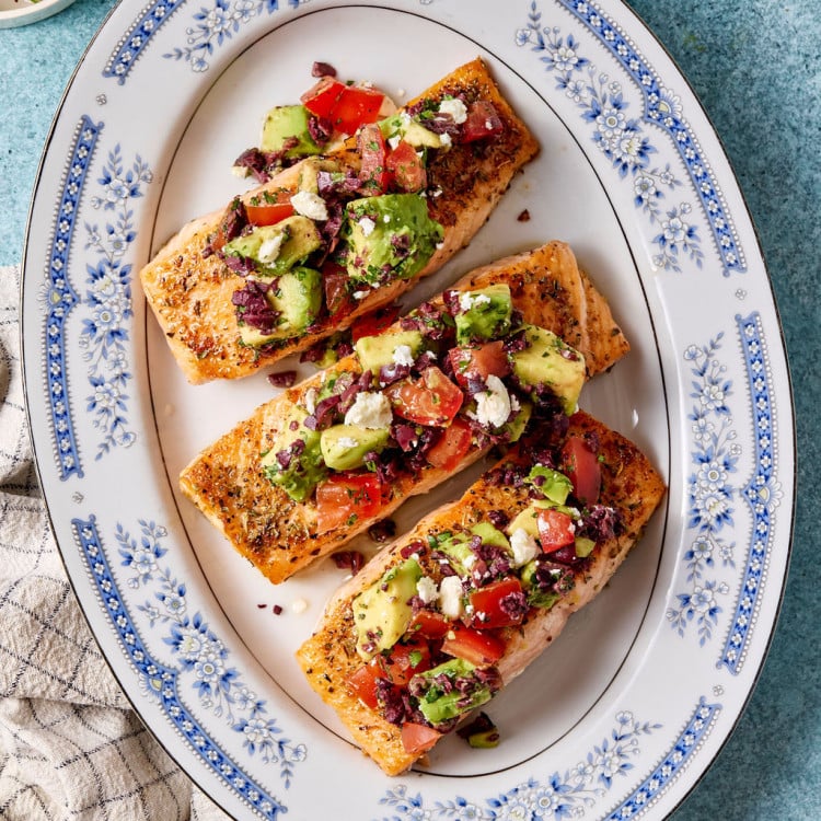 Mediterranean salmon fillets topped with avocado, tomato, olives, and feta arranged on a blue-and-white serving platter.