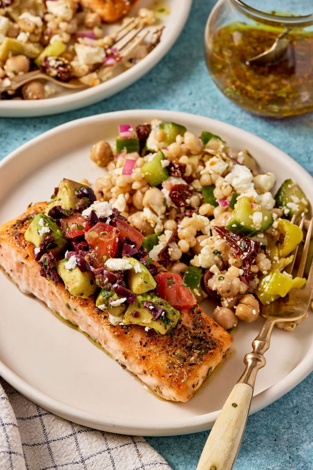 Close-up of Mediterranean salmon topped with avocado tomato olive salsa served with chickpea and couscous salad.