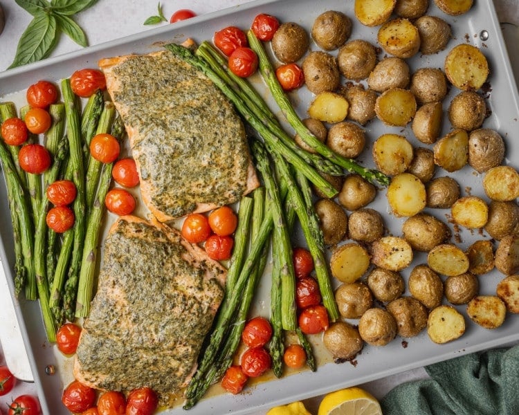 Sheet pan pesto salmon after baking with roasted asparagus, blistered cherry tomatoes, and crispy golden baby potatoes.