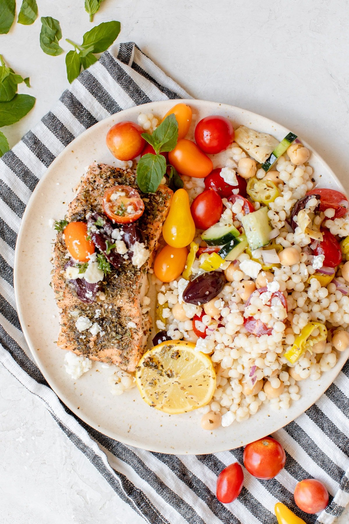 salmon with mediterranean flavors on a white plate with a pearl couscous salad