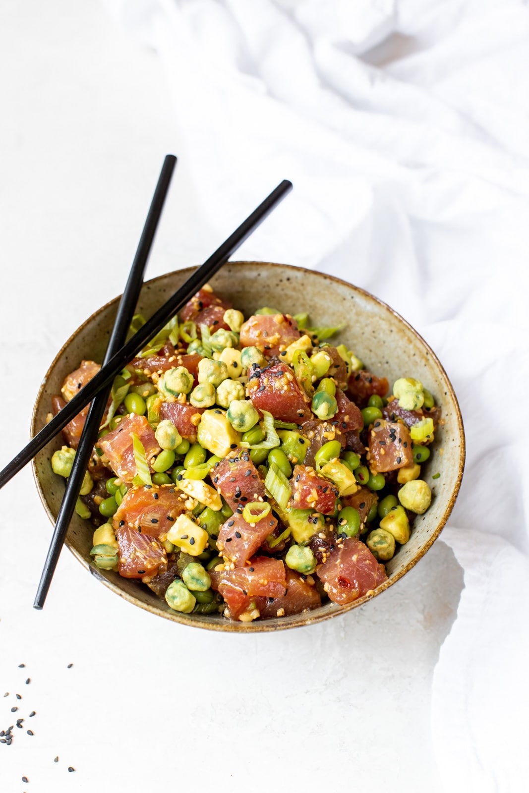 ahi poke in a brown bowl topped with green onions with black chopsticks