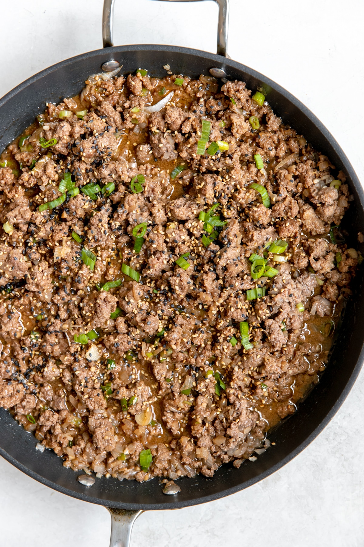 ground beef in a large black skillet with green onions on top