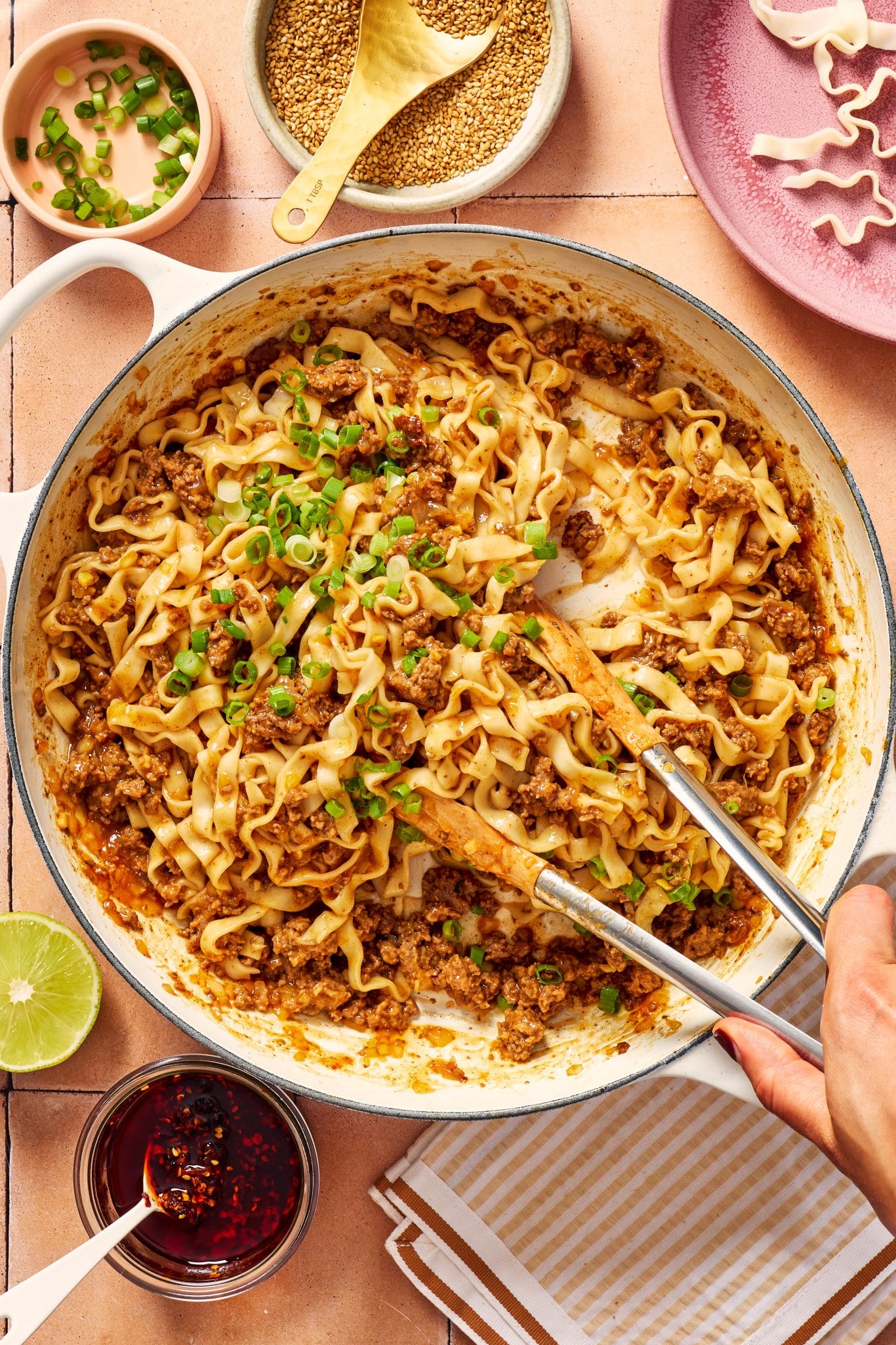 Saucy ground beef and noodles being tossed together in a large skillet with sliced green onions.