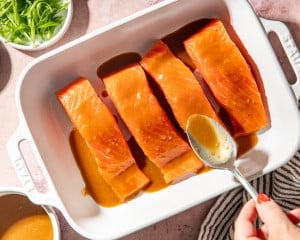Brown sugar miso glaze spooned evenly over fresh salmon fillets in a baking dish before marinating.