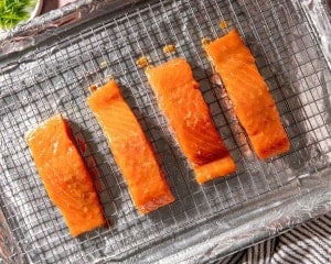 Marinated salmon fillets arranged on a wire rack set over a foil-lined baking sheet before baking.