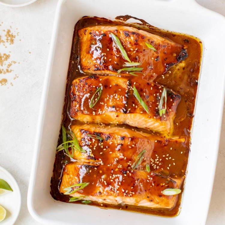 salmon in a white oven safe baking dish garnished with green onions and toasted sesame seeds