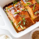 salmon in a white oven safe baking dish garnished with green onions and toasted sesame seeds