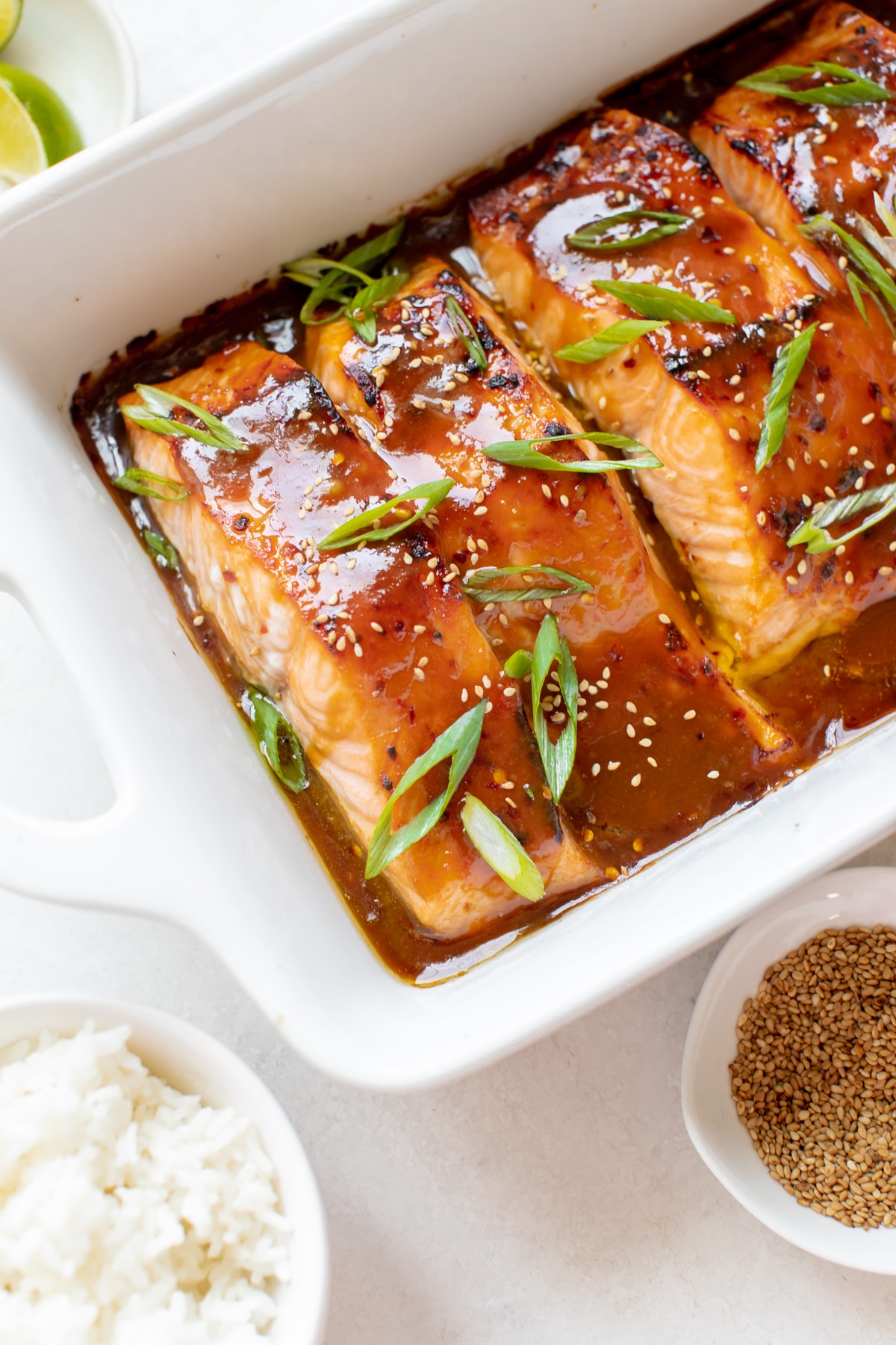 salmon in a white oven safe baking dish garnished with green onions and toasted sesame seeds