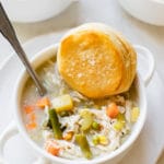 pot pie soup with chicken in a white soup bowl with a flaky biscuit on top