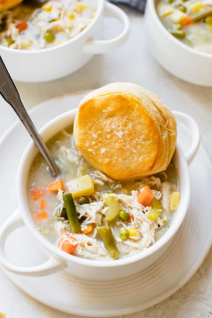 pot pie soup with chicken in a white soup bowl with a flaky biscuit on top