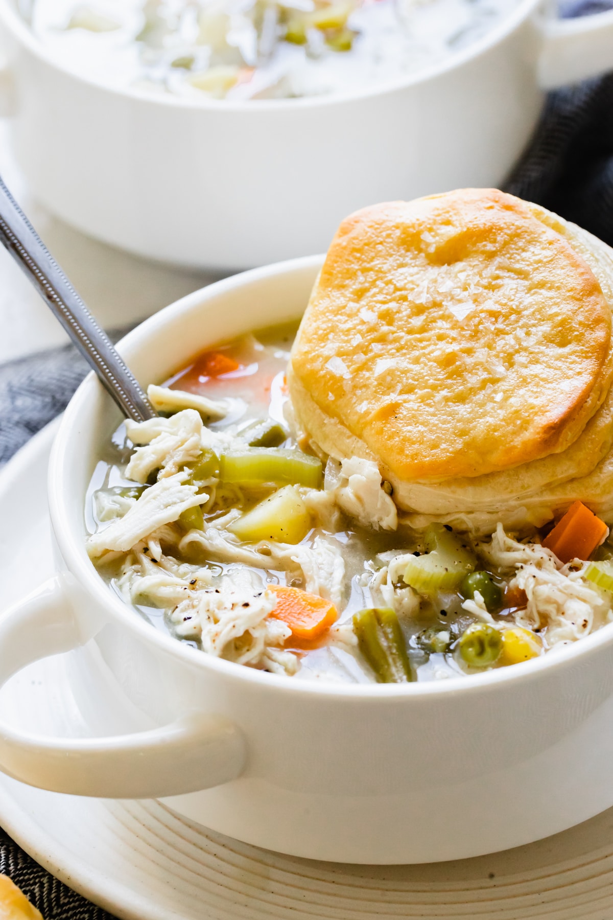 pot pie soup with chicken in a white soup bowl with a flaky biscuit on top