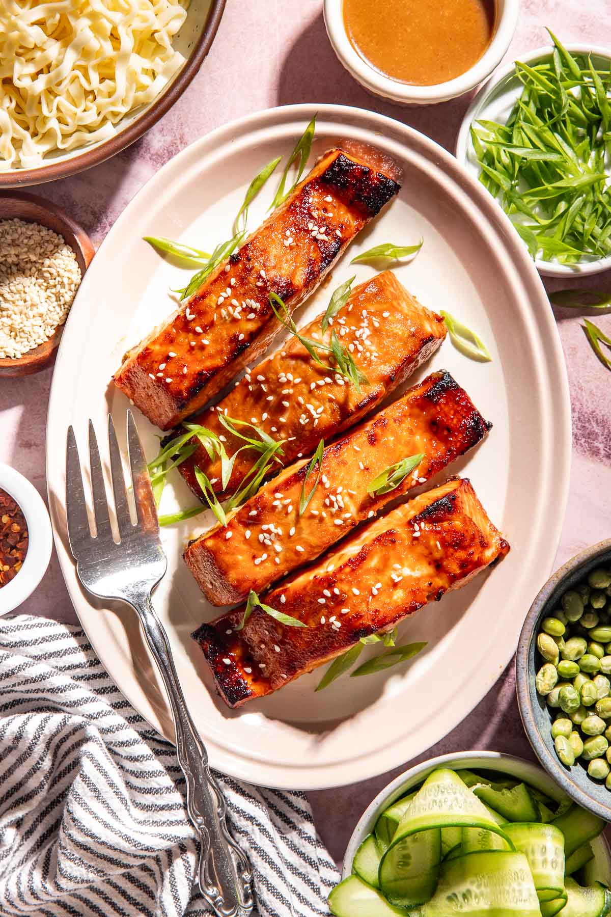 Brown sugar miso glazed salmon garnished with sesame seeds and sliced green onions, served with ramen noodles, edamame, cucumber ribbons, avocado, and extra miso glaze.