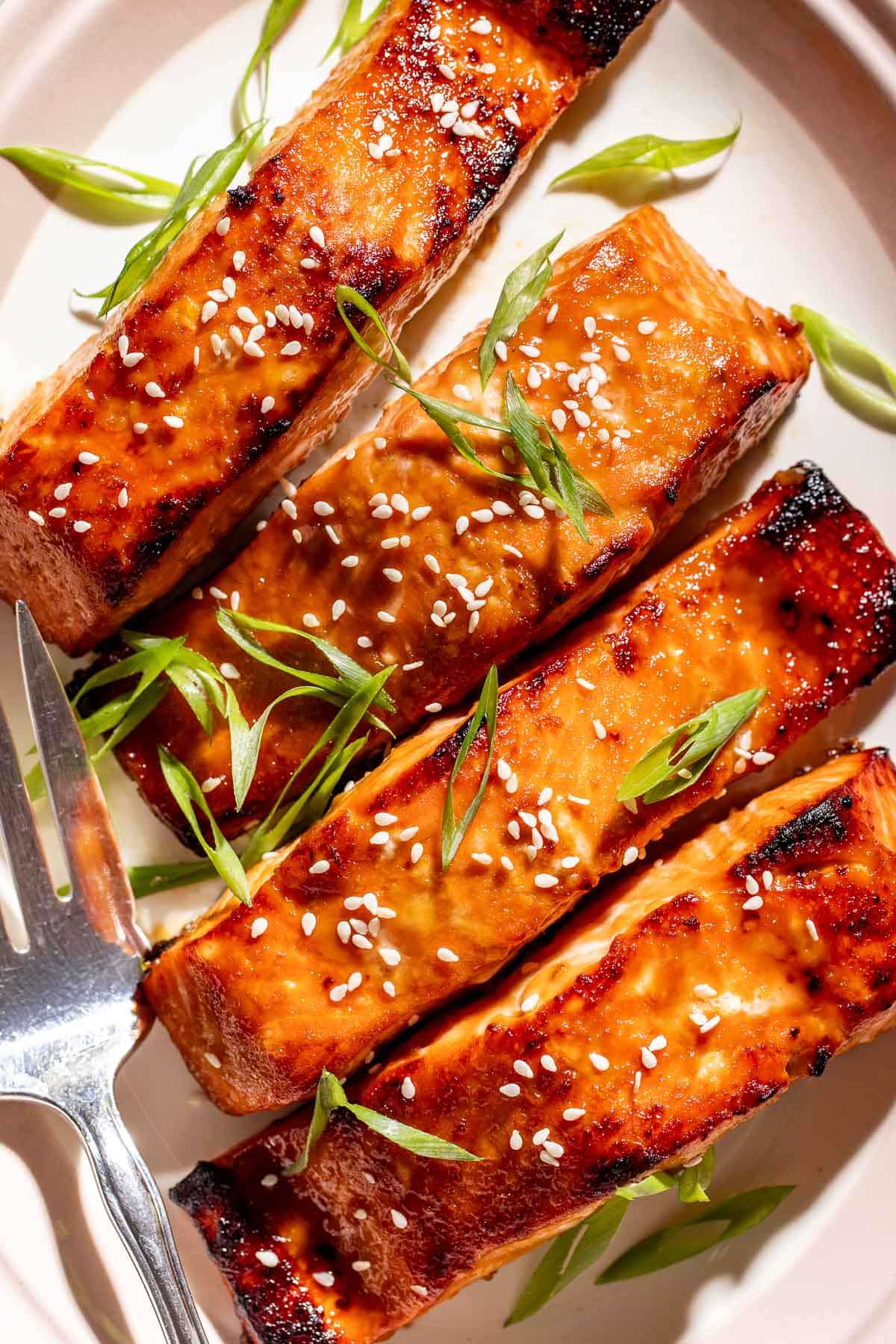 Close-up of caramelized brown sugar miso glazed salmon topped with sesame seeds and sliced green onions.