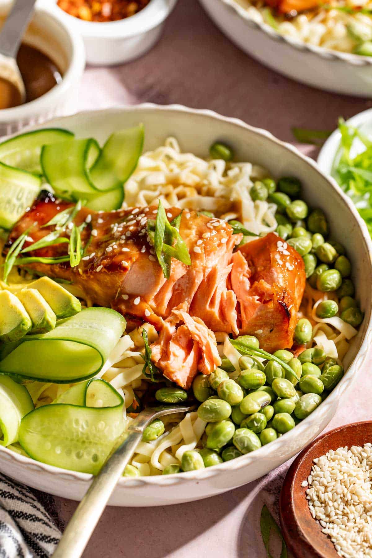 Flaked brown sugar miso glazed salmon served over ramen noodles with edamame, avocado, cucumber ribbons, sesame seeds, and sliced green onions.