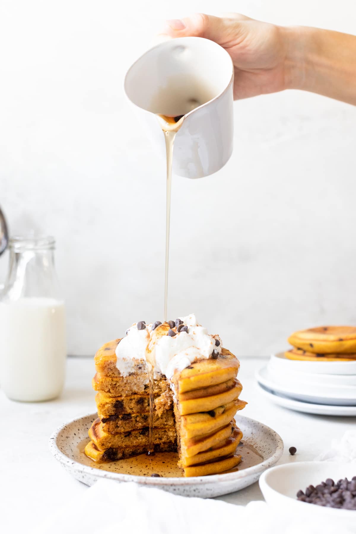 pancakes on a plate made with pumpkin topped with whipped cream and syrup being poured on the top