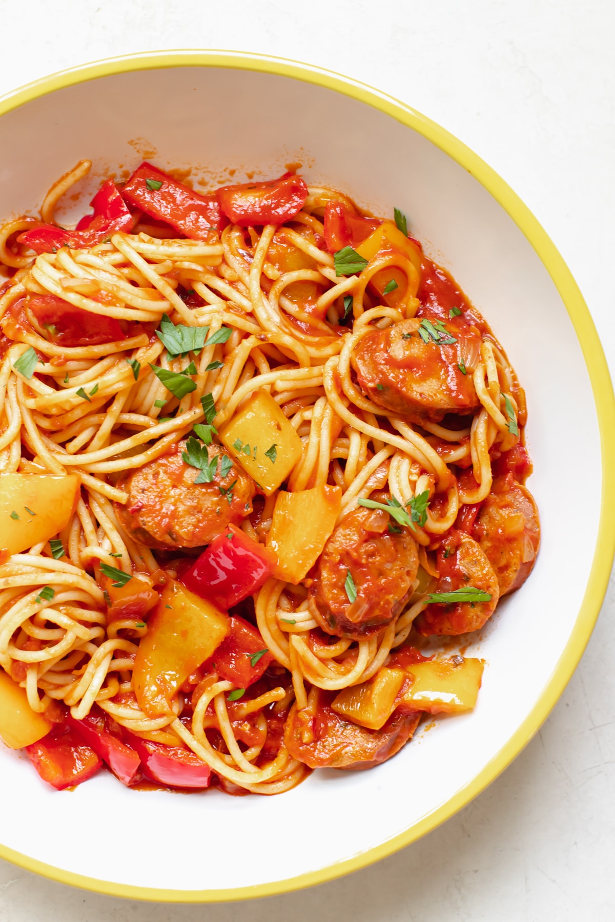 spaghetti and sausage in a white bowl topped with parsley