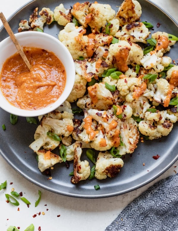 roasted cauliflower on a dark grey plate with miso sauce and green onions on top