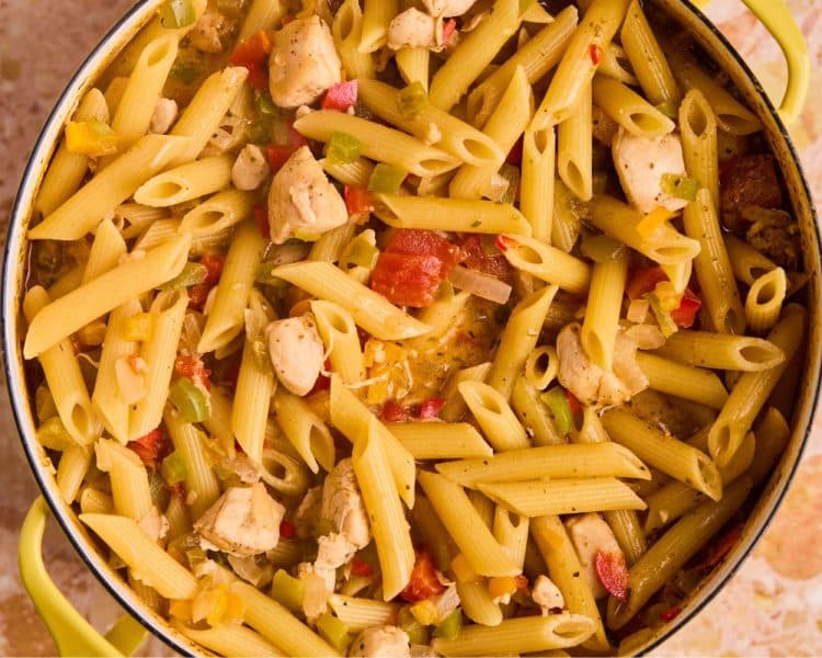 Dutch oven pot with cooked penne pasta, diced tomatoes, chopped bell peppers, and chopped onions.