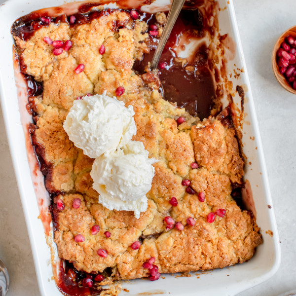 apple cobbler in a white baking dish topped with ice cream and pomegranate seeds