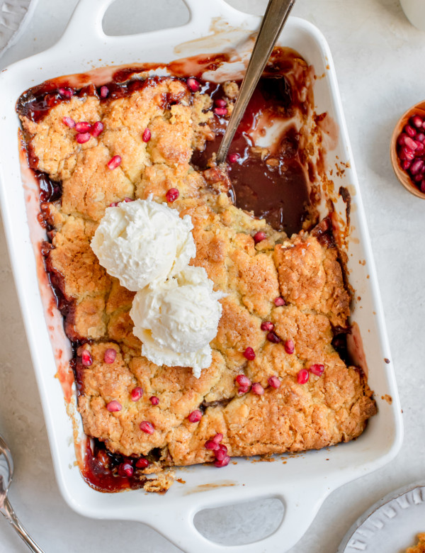 apple cobbler in a white baking dish topped with ice cream and pomegranate seeds