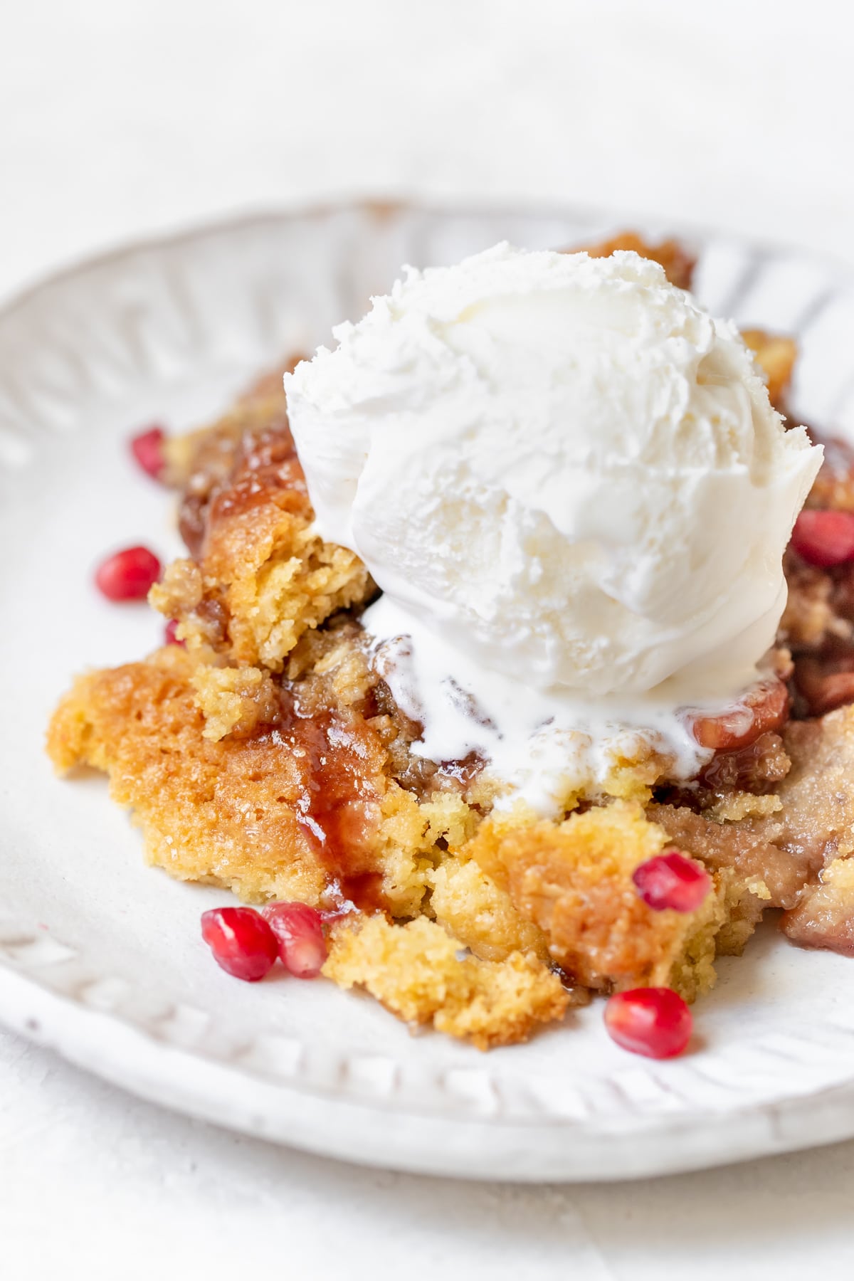 cobbler with apples and pomegranates on a white plate topped with vanilla bean ice cream