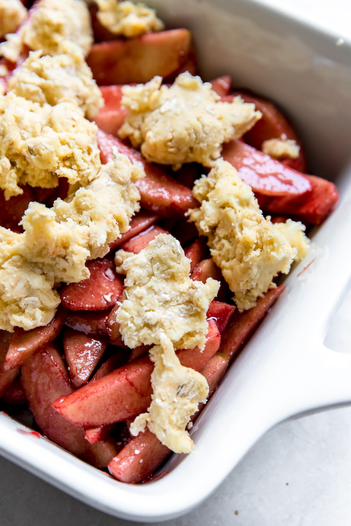 apples coated in a pomegranate reduction topped with cobbler topping in a white baking dish