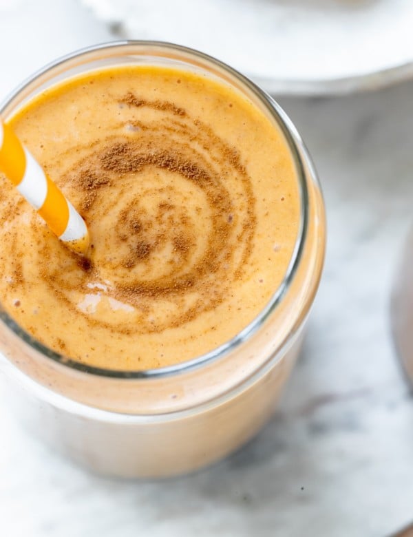 a smoothie made with pumpkin in a glass cup garnished with cinnamon and an orange straw