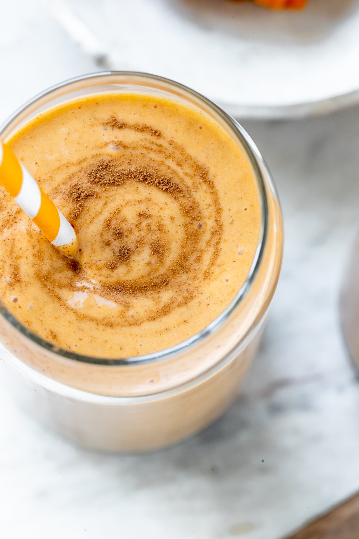 a smoothie made with pumpkin in a glass cup garnished with cinnamon and an orange straw