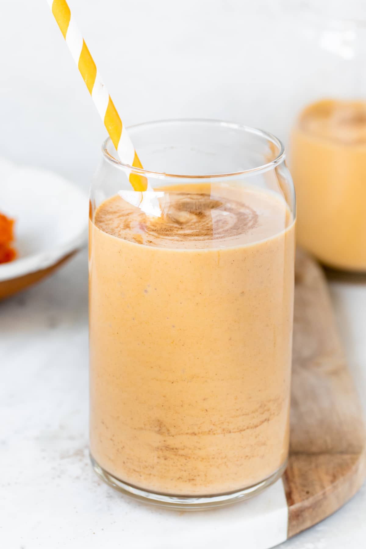 a smoothie made with pumpkin in a glass cup garnished with cinnamon and an orange straw