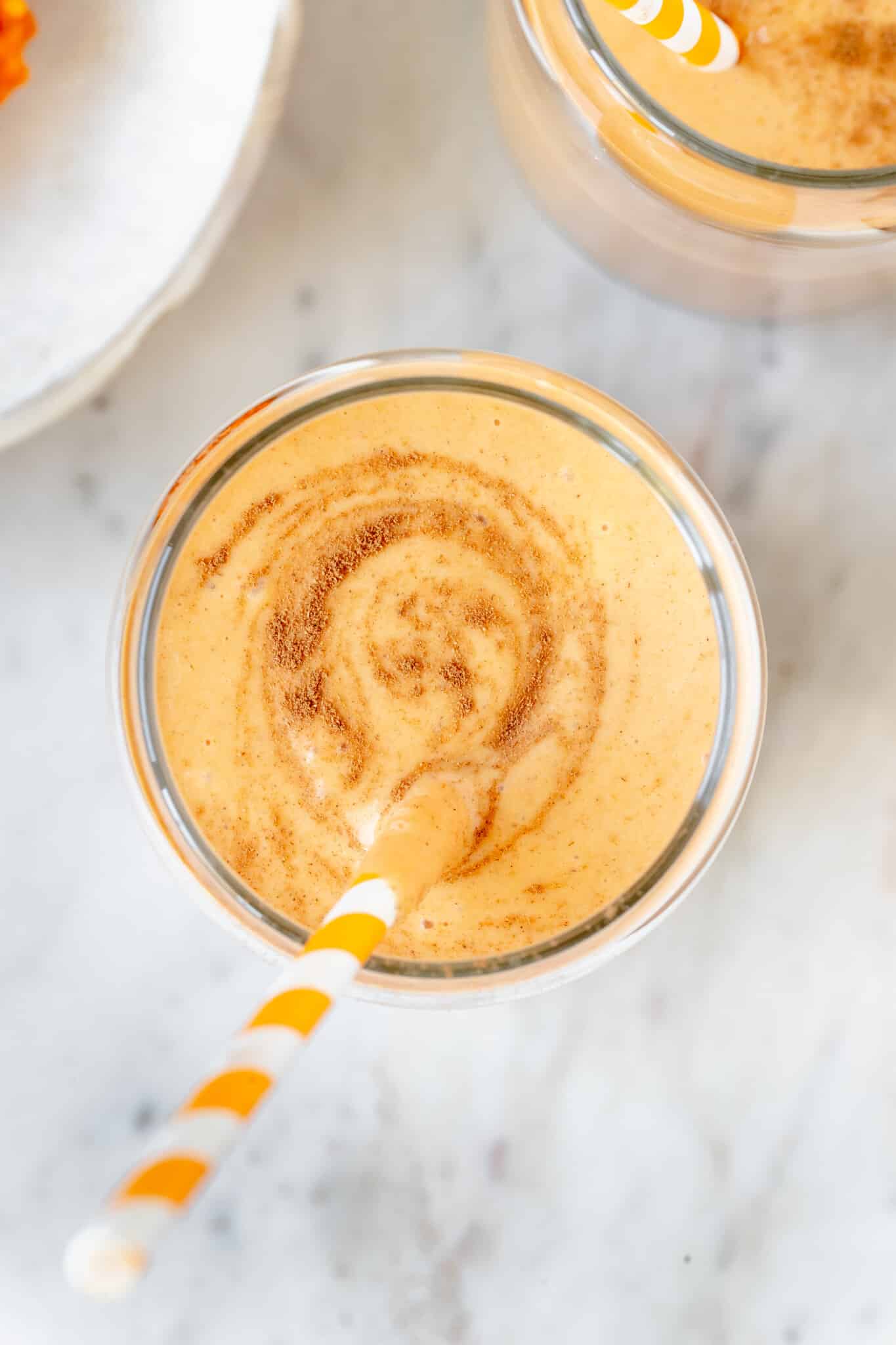 a smoothie made with pumpkin in a glass cup garnished with cinnamon and an orange straw