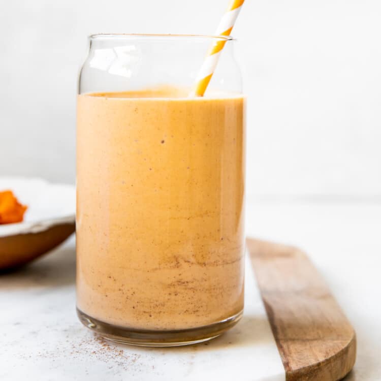 a smoothie made with pumpkin in a glass cup garnished with cinnamon and an orange straw