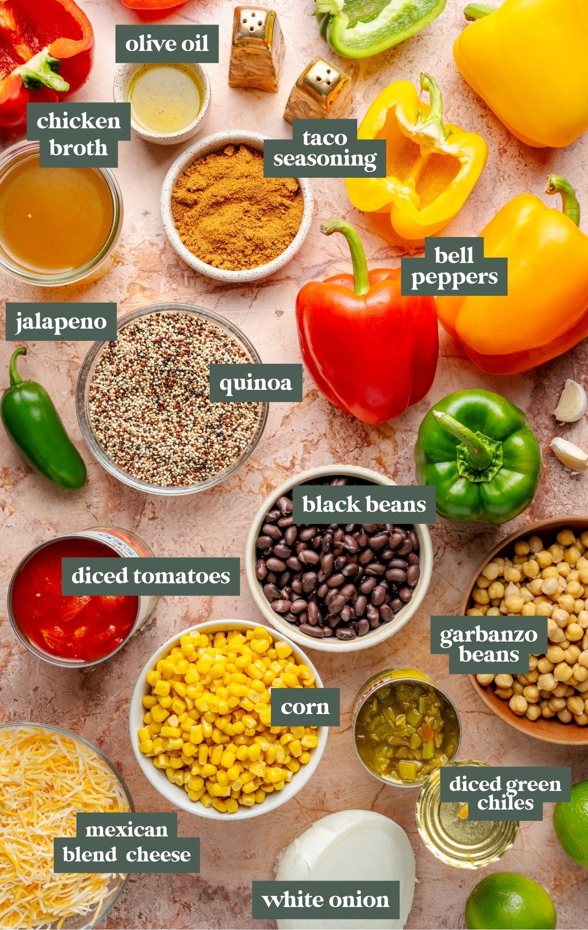 Flatlay of labeled ingredients for quinoa stuffed bell peppers, including: bell peppers, quinoa, black beans, garbanzo beans, corn, diced tomatoes, diced green chiles, white onion, Mexican blend cheese, jalapeño, taco seasoning, olive oil, and chicken broth. Ingredients are arranged around a light pink marbled surface.
