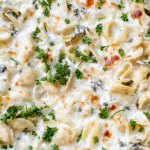baked pasta with spinach and artichokes covered in cheese and parsley