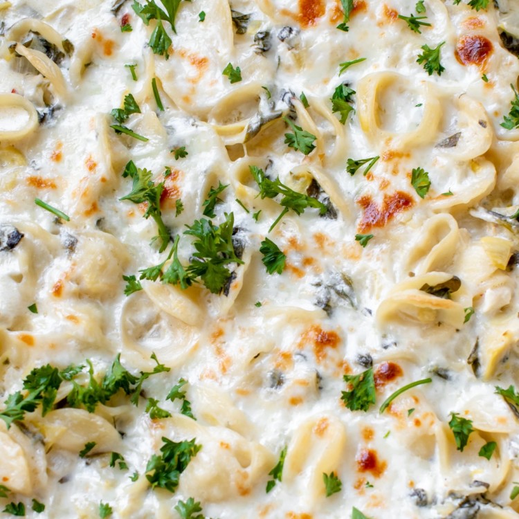 baked pasta with spinach and artichokes covered in cheese and parsley