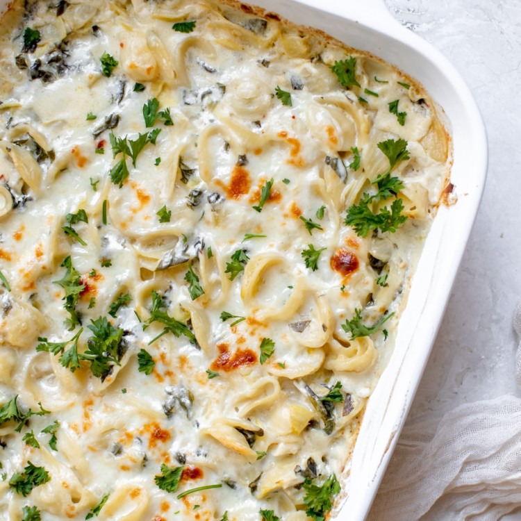 baked pasta with spinach and artichokes covered in cheese and parsley