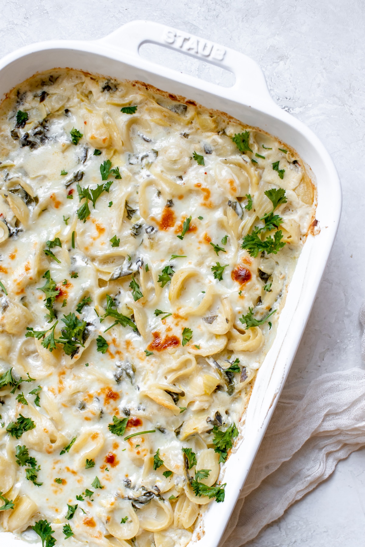 baked pasta with spinach and artichokes covered in cheese and parsley 