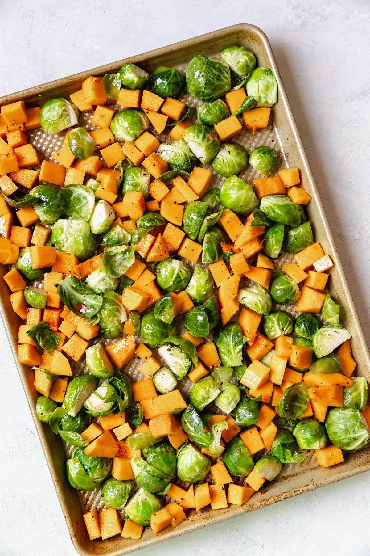 roasted brussels sprouts and butternut squash on a gold sheet pan tossed in olive oil, salt and pepper