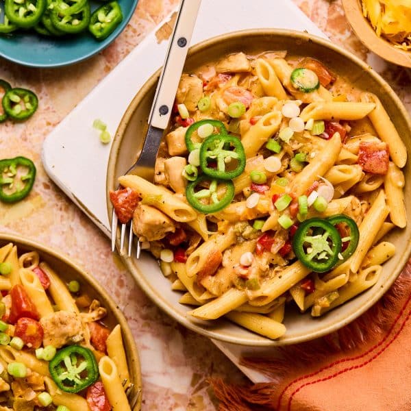 Bowl of penne pasta with cooked diced chicken, chopped bell pepper, chopped onions, creamy sauce, and topped with sliced jalapeno.